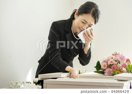 A woman in mourning who wipes tears in front of the casket A woman in mourning who wipes tears in front of the casket 84866429