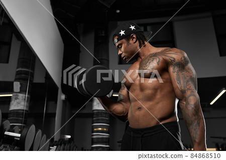 Strong and muscular dark skin man trains on modern equipment in gym. Portrait of muscular pumped up fitness trainer 84868510