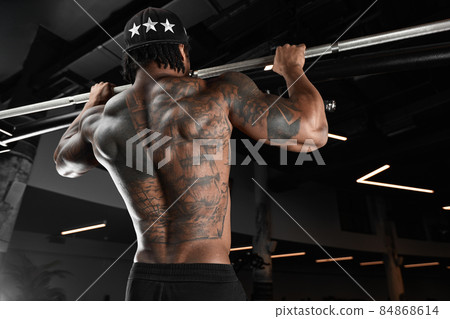 Strong and muscular dark skin man trains on modern equipment in gym. Portrait of muscular pumped up fitness trainer Strong and muscular dark skin man trains on modern equipment in gym. Portrait of muscular pumped up fitness trainer 84868614