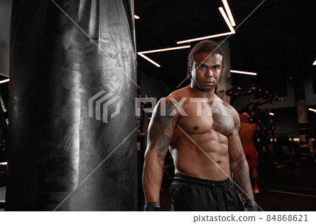 An African American guy trains in gym and fists his boxing bag fists. Concept of: gym, fitness, boxing, success, workout and power 84868621