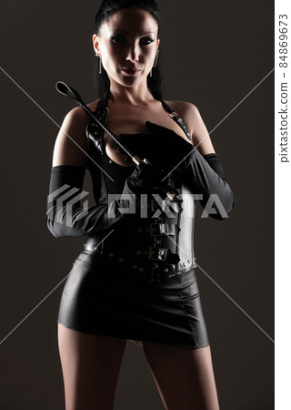 A young sexy woman in a black leather corset with open breasts poses with her hands covering her A young sexy woman in a black leather corset with open breasts poses with her hands covering her 84869673