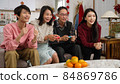son and daughter cheering for their parents who are playing exciting racing game with joysticks in the living room at home during chinese lunar new year holiday 84869786