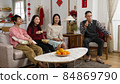 family eating snacks together at home during spring festival and watching a boring tv show chosen by the happy mother who's talking with gestures. chinese text translation: spring and congratulation 84869790