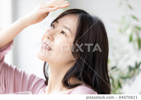 一個身著房間的女人站在窗邊，拿著一杯水 84870821