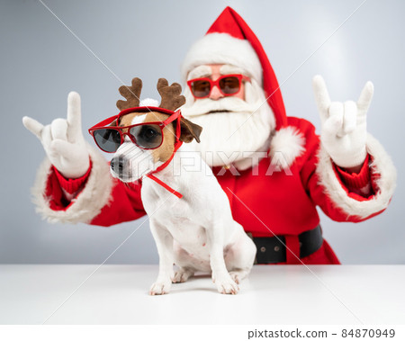 Santa claus and santa's helper in sunglasses on a white background. Jack russell terrier dog in a deer costume Santa claus and santa's helper in sunglasses on a white background. Jack russell terrier dog in a deer costume 84870949
