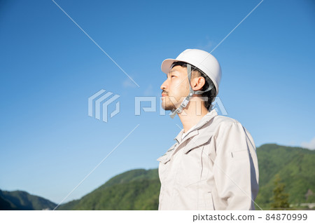 Image of a man in work clothes looking up at the blue sky 84870999