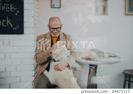 Happy senior man sitting in cafeteria and playing with his dog, shot through glass. 84871315