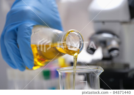A hand in a glove pours a yellow liquid in the laboratory A hand in a glove pours a yellow liquid in the laboratory 84871440