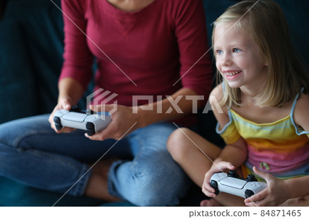 A little girl with a nanny sits on the couch plays a video gam A little girl with a nanny sits on the couch plays a video gam 84871465