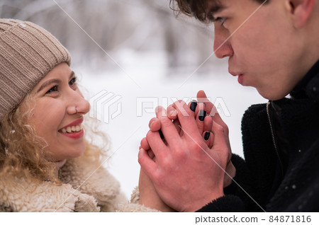 A young couple walks in the winter in the forest. The guy warms the girl's hands. A young couple walks in the winter in the forest. The guy warms the girl's hands. 84871816