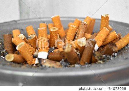 Used yellow cigarette butts on a round stainless metal ashtray 84872066