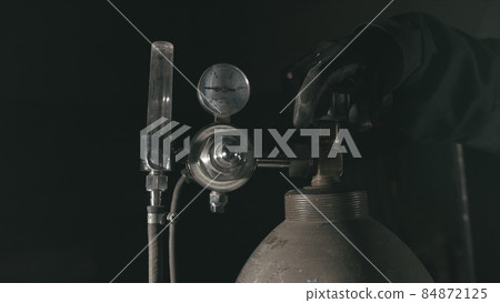 Forge workshop. Smithy manual production. A worker open gas cylinder vessel with oxygen for welding. Cinematic black look. Forge workshop. Smithy manual production. A worker open gas cylinder vessel with oxygen for welding. Cinematic black look. 84872125