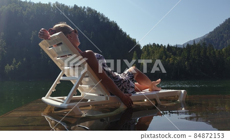Woman lie on a sunbed in sunglasses and a boho silk shawl. Girl rest on a flood wood underwater pier. The pavement is covered with water in the lake. Woman lie on a sunbed in sunglasses and a boho silk shawl. Girl rest on a flood wood underwater pier. The pavement is covered with water in the lake. 84872153