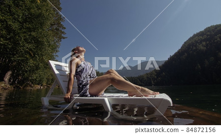 Woman lie on a sunbed in sunglasses and a boho silk shawl. Girl rest on a flood wood underwater pier. The pavement is covered with water in the lake. Woman lie on a sunbed in sunglasses and a boho silk shawl. Girl rest on a flood wood underwater pier. The pavement is covered with water in the lake. 84872156