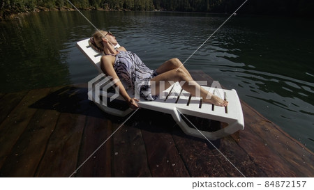 Woman lie on a sunbed in sunglasses and a boho silk shawl. Girl rest on a flood wood underwater pier. The pavement is covered with water in the lake. Woman lie on a sunbed in sunglasses and a boho silk shawl. Girl rest on a flood wood underwater pier. The pavement is covered with water in the lake. 84872157