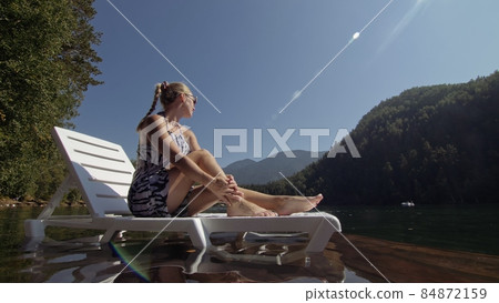 Woman lie on a sunbed in sunglasses and a boho silk shawl. Girl rest on a flood wood underwater pier. The pavement is covered with water in the lake. Woman lie on a sunbed in sunglasses and a boho silk shawl. Girl rest on a flood wood underwater pier. The pavement is covered with water in the lake. 84872159