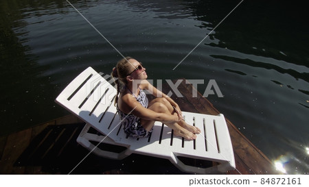 Woman lie on a sunbed in sunglasses and a boho silk shawl. Girl rest on a flood wood underwater pier. The pavement is covered with water in the lake. Woman lie on a sunbed in sunglasses and a boho silk shawl. Girl rest on a flood wood underwater pier. The pavement is covered with water in the lake. 84872161