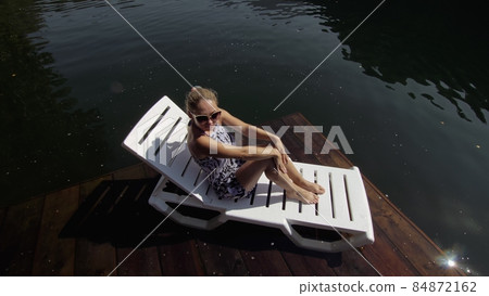 Woman lie on a sunbed in sunglasses and a boho silk shawl. Girl rest on a flood wood underwater pier. The pavement is covered with water in the lake. Woman lie on a sunbed in sunglasses and a boho silk shawl. Girl rest on a flood wood underwater pier. The pavement is covered with water in the lake. 84872162