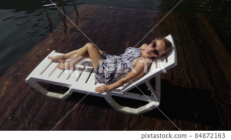 Woman lie on a sunbed in sunglasses and a boho silk shawl. Girl rest on a flood wood underwater pier. The pavement is covered with water in the lake. Woman lie on a sunbed in sunglasses and a boho silk shawl. Girl rest on a flood wood underwater pier. The pavement is covered with water in the lake. 84872163