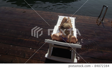 Woman lie on a sunbed in sunglasses and a boho silk shawl. Girl rest on a flood wood underwater pier. The pavement is covered with water in the lake. Woman lie on a sunbed in sunglasses and a boho silk shawl. Girl rest on a flood wood underwater pier. The pavement is covered with water in the lake. 84872164