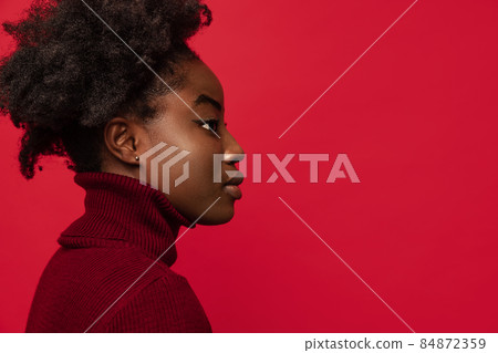 Side view of beautiful African young woman looking straight isolated on dark red studio background. 84872359