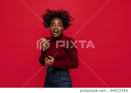 Portrait of dark skinned young pretty girl wondering isolated on dark red studio background. 84872364