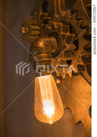 Steampunk architectural style design element of interior.Lamp bulbs fixed on iron industrial gear cogwheels sprocket lighting illuminated equipment Steampunk architectural style design element of interior.Lamp bulbs fixed on iron industrial gear cogwheels sprocket lighting illuminated equipment 84872667