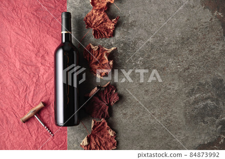 Bottle of red wine with corkscrew and dried vine leaves. Bottle of red wine with corkscrew and dried vine leaves. 84873992