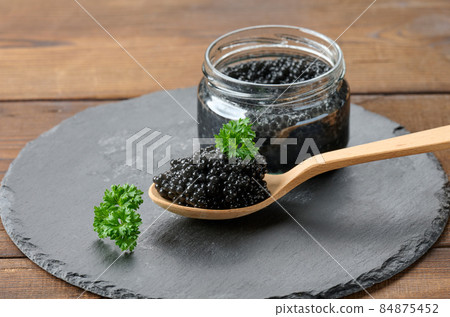 fresh grainy black paddlefish caviar in brown wooden spoon on a brown table, close up fresh grainy black paddlefish caviar in brown wooden spoon on a brown table, close up 84875452