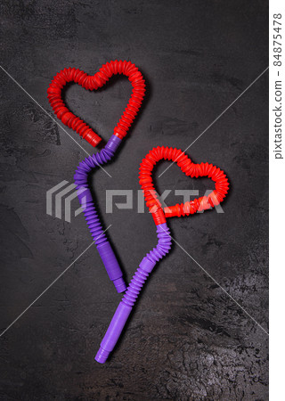 Tube toys bent as two red heart balloons and wavy ribbons on black Tube toys bent as two red heart balloons and wavy ribbons on black 84875478