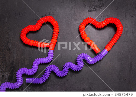 Tube toys bent as two red heart balloons and wavy ribbons on black background Tube toys bent as two red heart balloons and wavy ribbons on black background 84875479