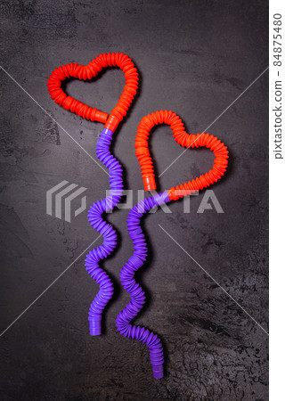 Tube toys bent as two red heart balloons and wavy ribbons on black Tube toys bent as two red heart balloons and wavy ribbons on black 84875480