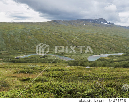 Valley with winding Laddejahka river, mountain hut STF Laddejahka fjallstuga cabin, birch tree forest and green mountains. Lapland landscape Sweden at Padjelantaleden hiking trail. Summer moody sky 84875728