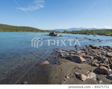 View of turquoise blue water of wild Vuojatadno river. Northern landscape in Swedish Lapland with birch tree forest and green mountains at Padjelantaleden hiking trail. Summer sunny day, blue sky View of turquoise blue water of wild Vuojatadno river. Northern landscape in Swedish Lapland with birch tree forest and green mountains at Padjelantaleden hiking trail. Summer sunny day, blue sky 84875752