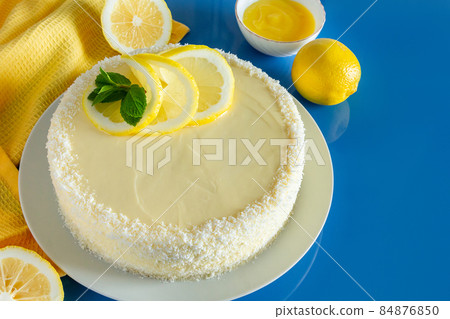 Lemon cake with coconut flakes on a blue background. Delicate dessert with cream. 84876850