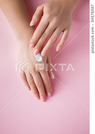 A young woman is applying cream to her hands. Spa and body care concept on pink background. Place for text. 84876887