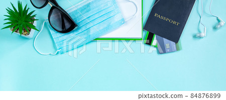 Safe travel concept during the coronavirus pandemic. Passport, medical mask and sunglasses on a blue background. Flatlay, banner format. 84876899
