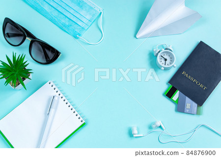 Safe travel concept during the coronavirus pandemic. Passport, medical mask and sunglasses on a blue background. Flatlay, banner format. 84876900