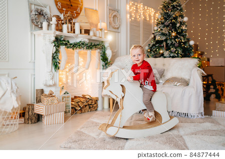 cute little boy on rocking horse in room with fireplace and christmas tree. 84877444
