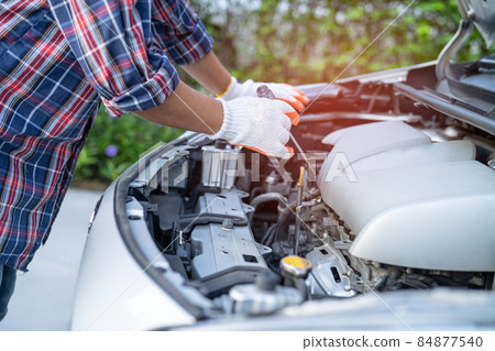 Asian auto mechanic check for repair under the hood of broken down car on the side of the road. 84877540