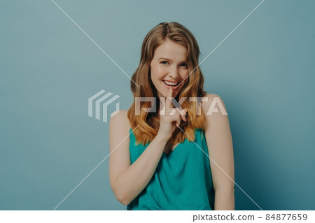 Flirty young woman shows silence Shhh symbol with index finger touching her lip, isolated on blue Flirty young woman shows silence Shhh symbol with index finger touching her lip, isolated on blue 84877659