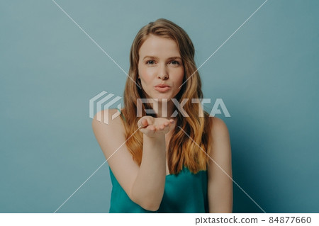 Pretty candid girl blowing air kiss and expressing love while standing isolated on blue background 84877660