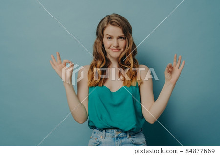 Confident joyful young woman in casual clothes gesturing ok sign with both hands in studio Confident joyful young woman in casual clothes gesturing ok sign with both hands in studio 84877669