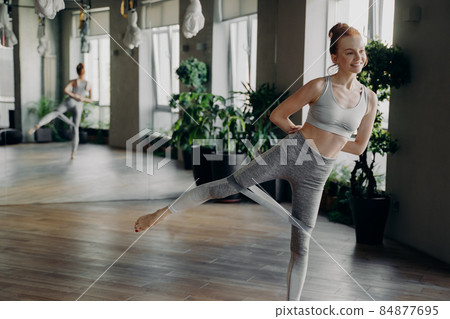 Athletic slender red haired woman during her fitness workout with rubber resistance band 84877695