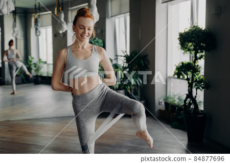 Slim pretty fitness woman with red hair doing leg exercise with rubber resistance band Slim pretty fitness woman with red hair doing leg exercise with rubber resistance band 84877696