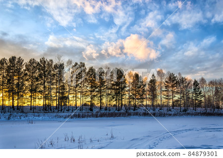 Gentle sunset over the trees and the snow-covered river. Beautiful clouds illuminated by the evening sun. Nature of Eastern Siberia Gentle sunset over the trees and the snow-covered river. Beautiful clouds illuminated by the evening sun. Nature of Eastern Siberia 84879301