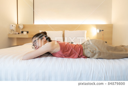 Young Asian woman sleeping on comfortable bed in cozy style hotel bedroom. Sleep is essential for strong health and well-being. 84879800