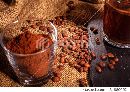 on a stone black stand, black coffee in a glass Cup against a background of burlap. next to sugar, coffee beans and ground coffee. 84880062