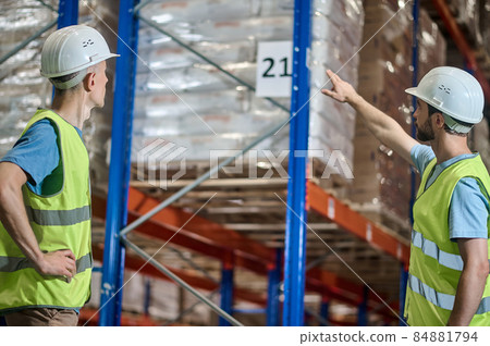 Man in overalls showing colleague number on warehouse shelf Man in overalls showing colleague number on warehouse shelf 84881794