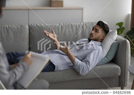 Depressed arab man lying on couch at psychologist's office, having session with counselor, seeking professional help 84882696